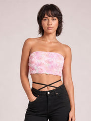 Model poses in black jeans wearing a fitted pink floral-detail cropped tube top with a strapless straight neckline and exposed midriff.