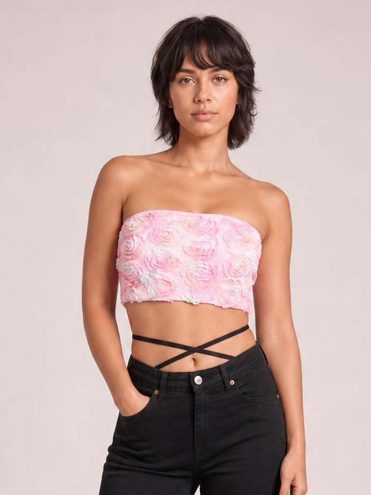 Model poses in black jeans wearing a fitted pink floral-detail cropped tube top with a strapless straight neckline and exposed midriff.