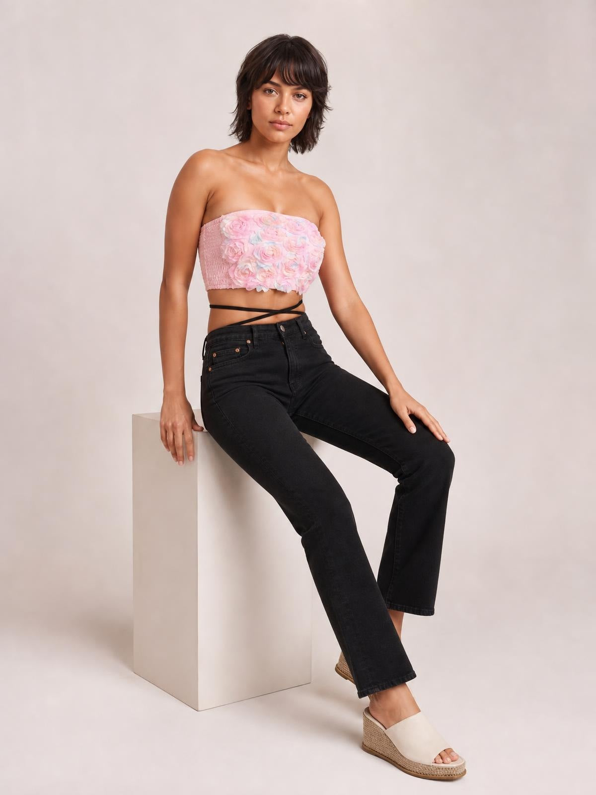 A model sits in a relaxed pose wearing a pink floral detail cropped tube top with a strapless neckline, fitted silhouette, and textured sides.