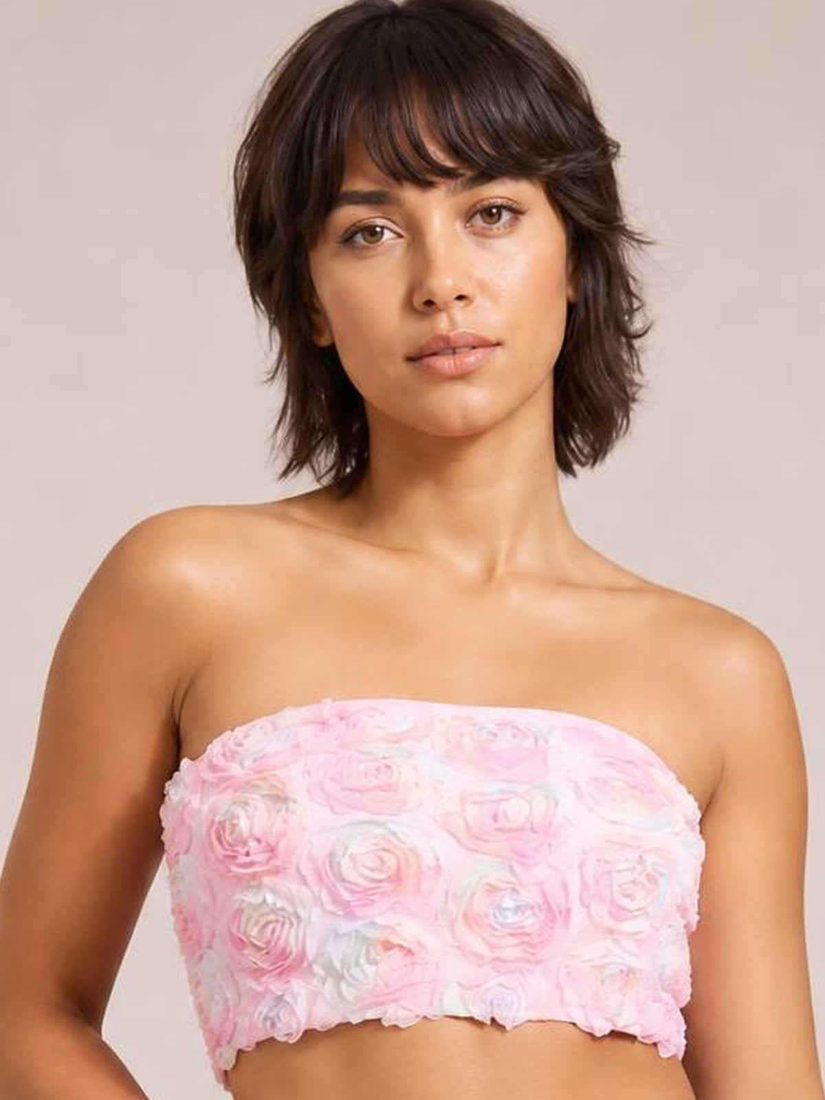 Model wearing a pink cropped tube top with raised floral rosette detail, a strapless neckline, fitted silhouette, and softly scalloped hem.