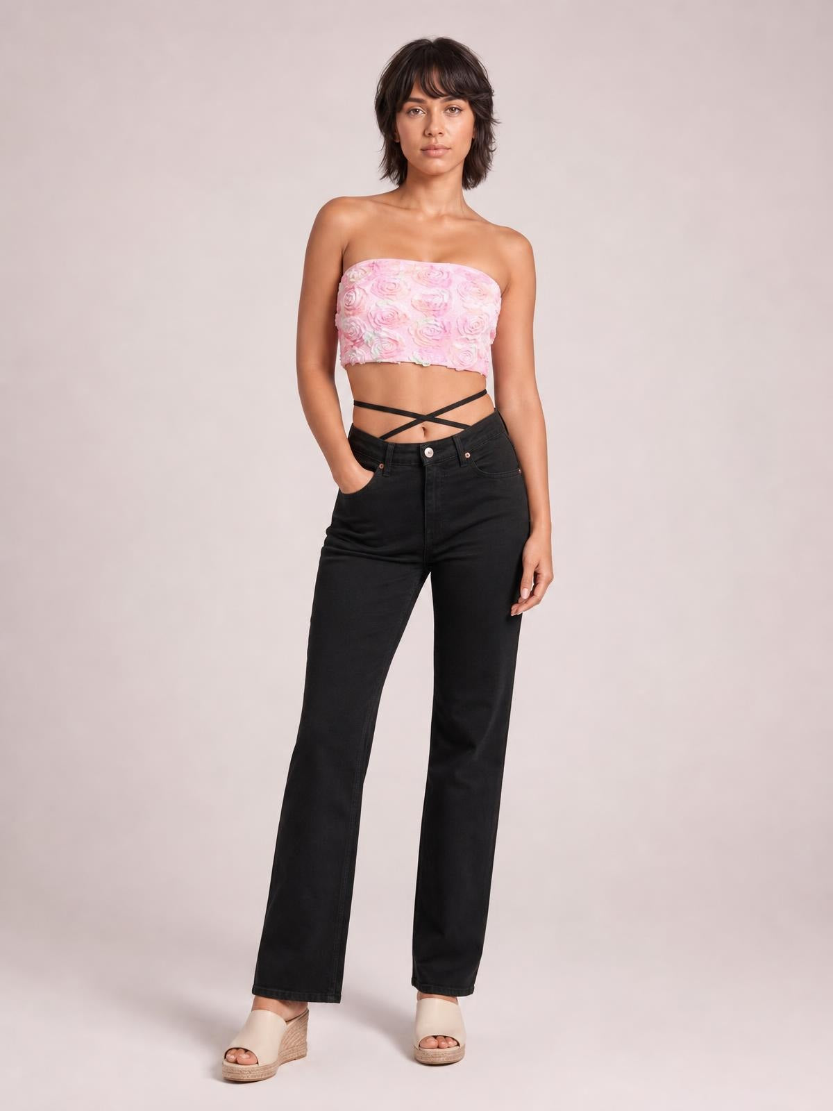 Model poses in a pink floral-detail cropped tube top with a straight neckline and fitted silhouette, paired with high-waisted black wide-leg jeans.