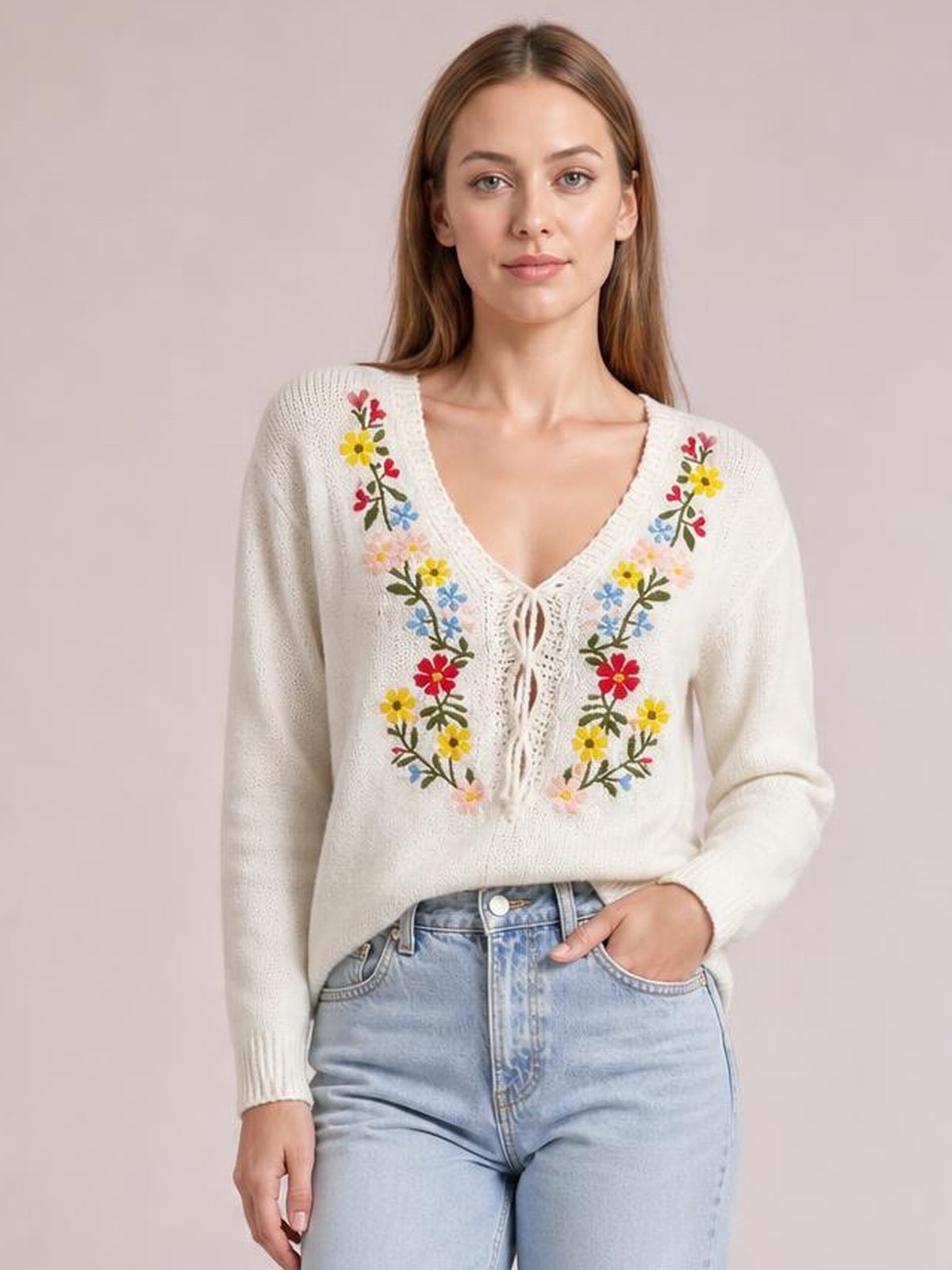 Model wearing an ivory floral embroidered V-neck sweater with long sleeves, a relaxed silhouette, ribbed cuffs, and a tied openwork front detail.