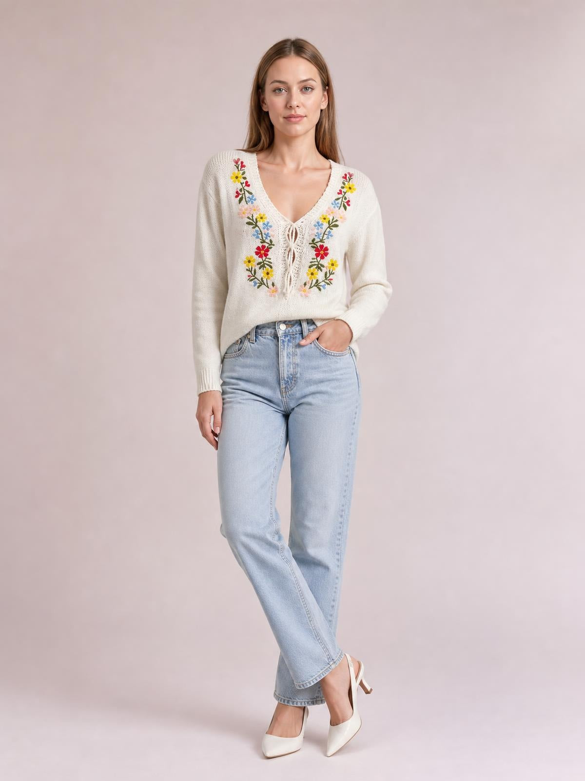 Model poses in a cream floral embroidered V-neck sweater with a tied front, long sleeves, ribbed cuffs, and a relaxed silhouette.