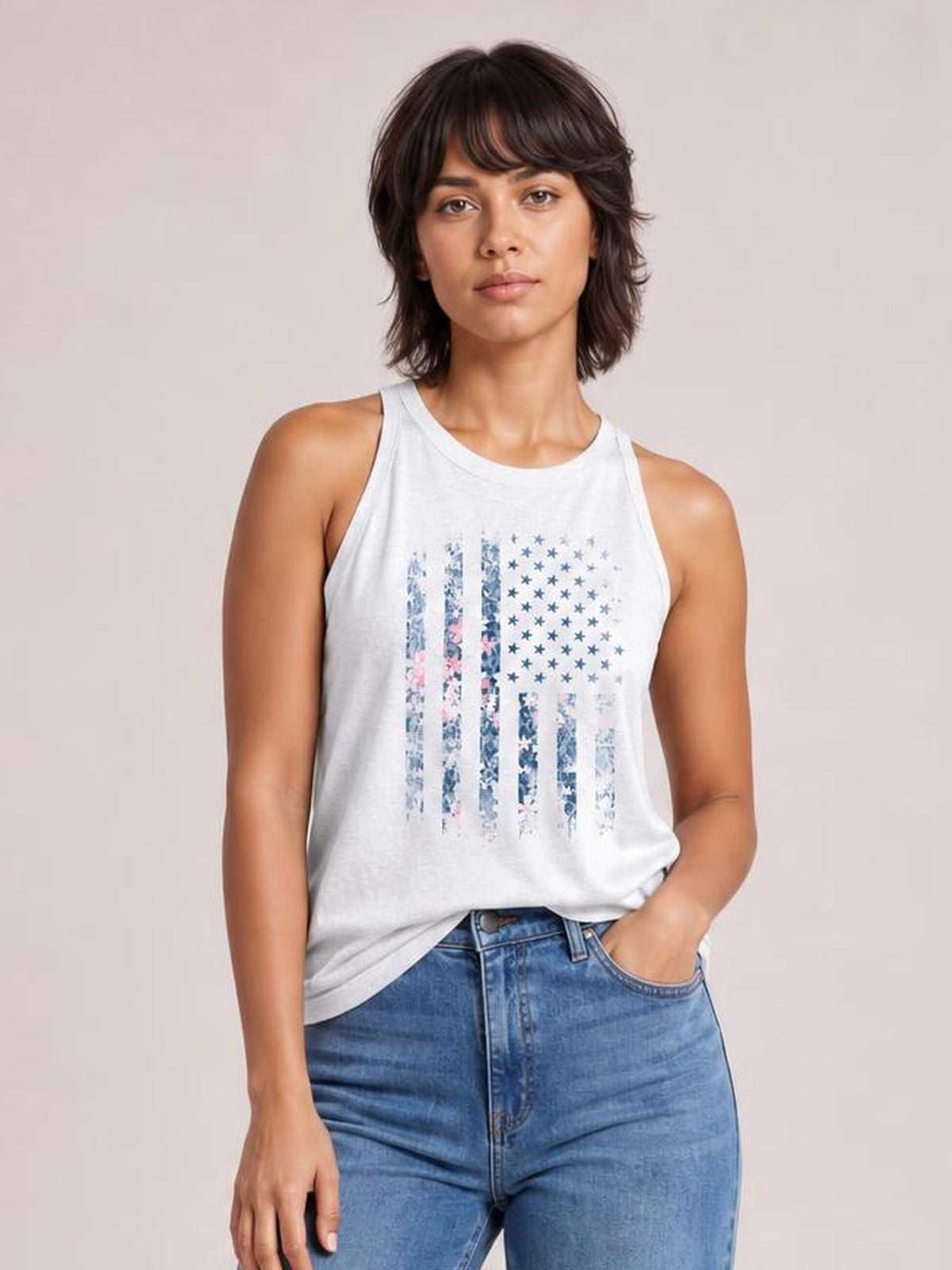Model poses in a white sleeveless tank with a floral graphic, round Grecian-style neckline, regular relaxed silhouette, and one hand in her jeans pocket.