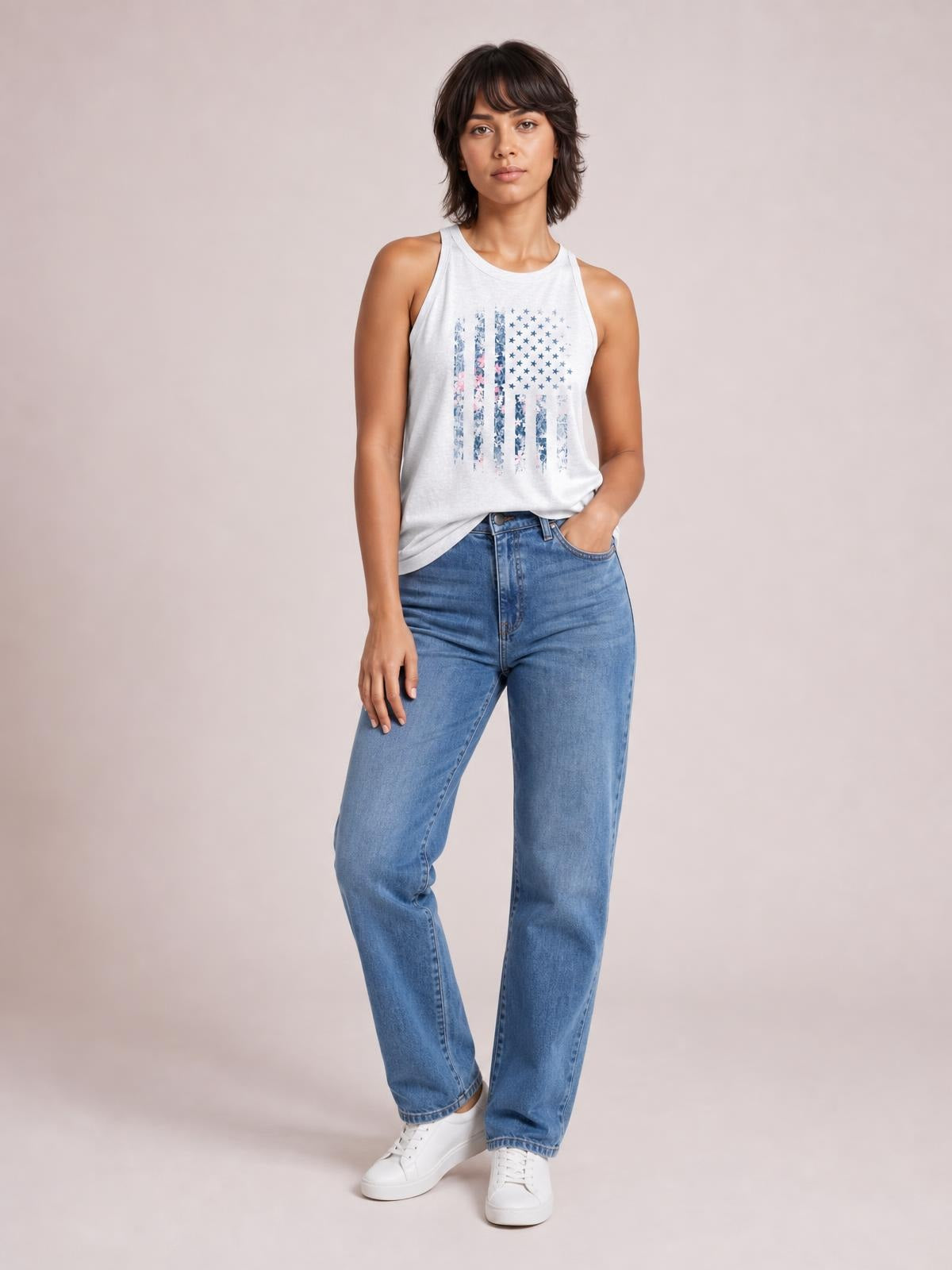 Model wearing a light gray floral graphic Grecian neck tank with a sleeveless, regular-length silhouette, standing casually with one hand in her jeans pocket.