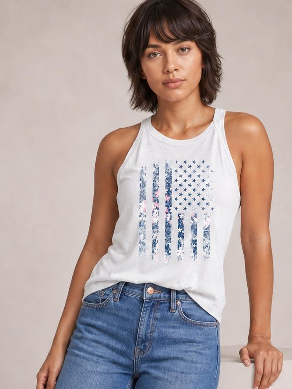 Model wears a white floral graphic Grecian neck tank with a rounded neckline, sleeveless cut, and relaxed regular-length silhouette, paired with jeans.