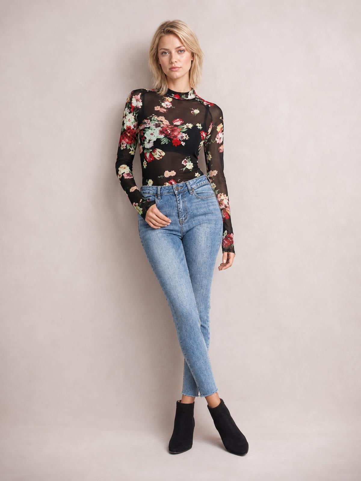 Model poses in a black floral mock neck long sleeve top with a fitted silhouette, sheer sleeves, and a tucked hem.