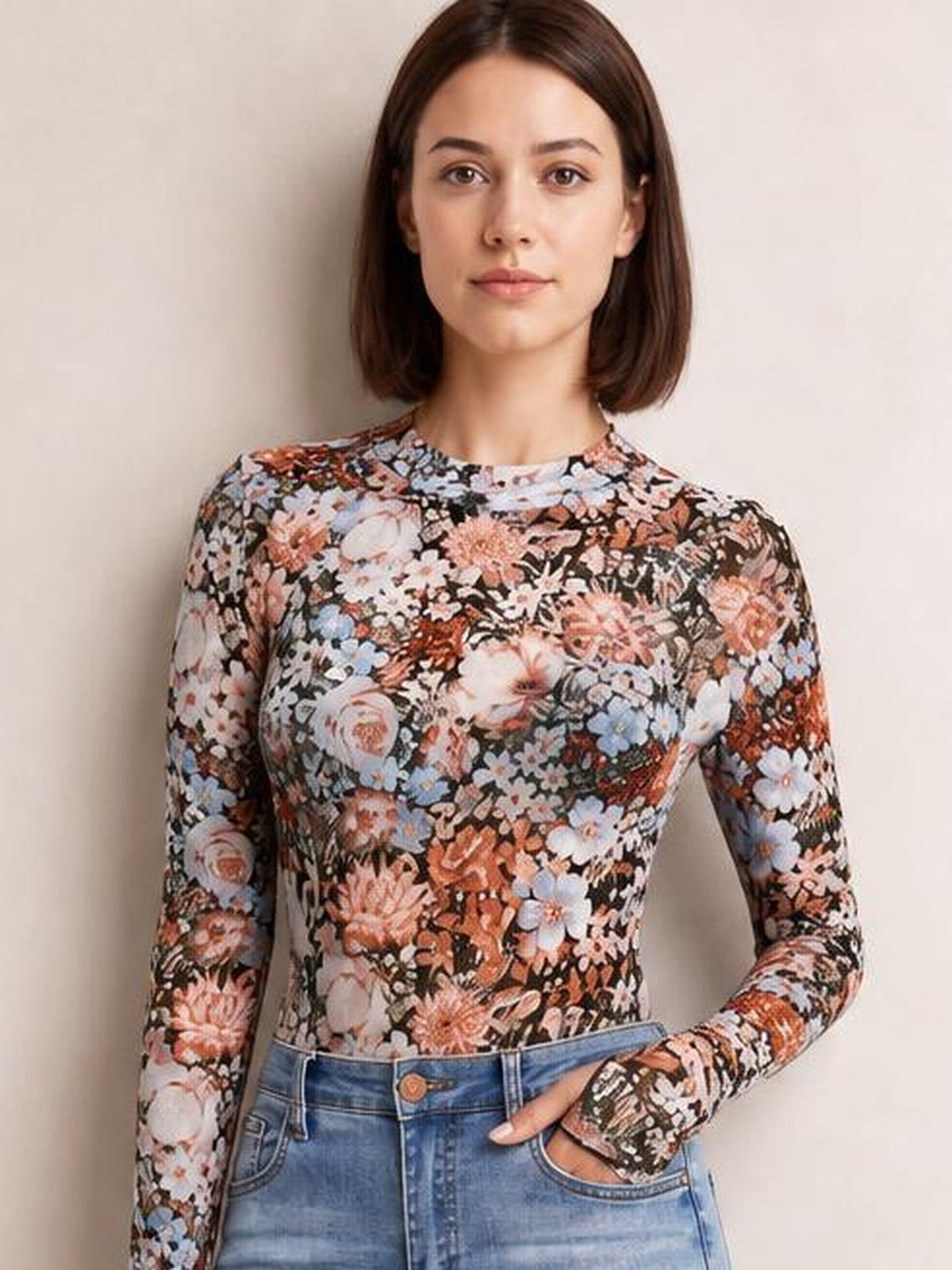 Model stands with one hand in her jeans pocket, wearing a fitted floral mock neck top with long sleeves and multicolor blooms on a dark background.