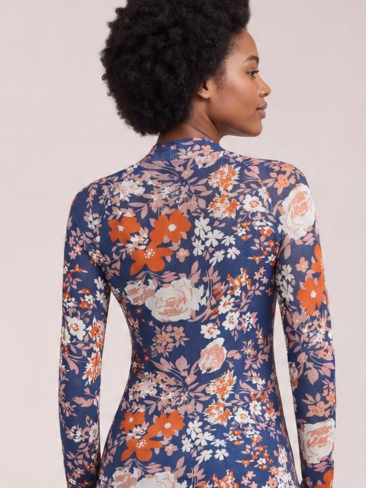 A woman in side profile wears a navy floral mock neck long sleeve top with a fitted silhouette and colorful allover flower print.