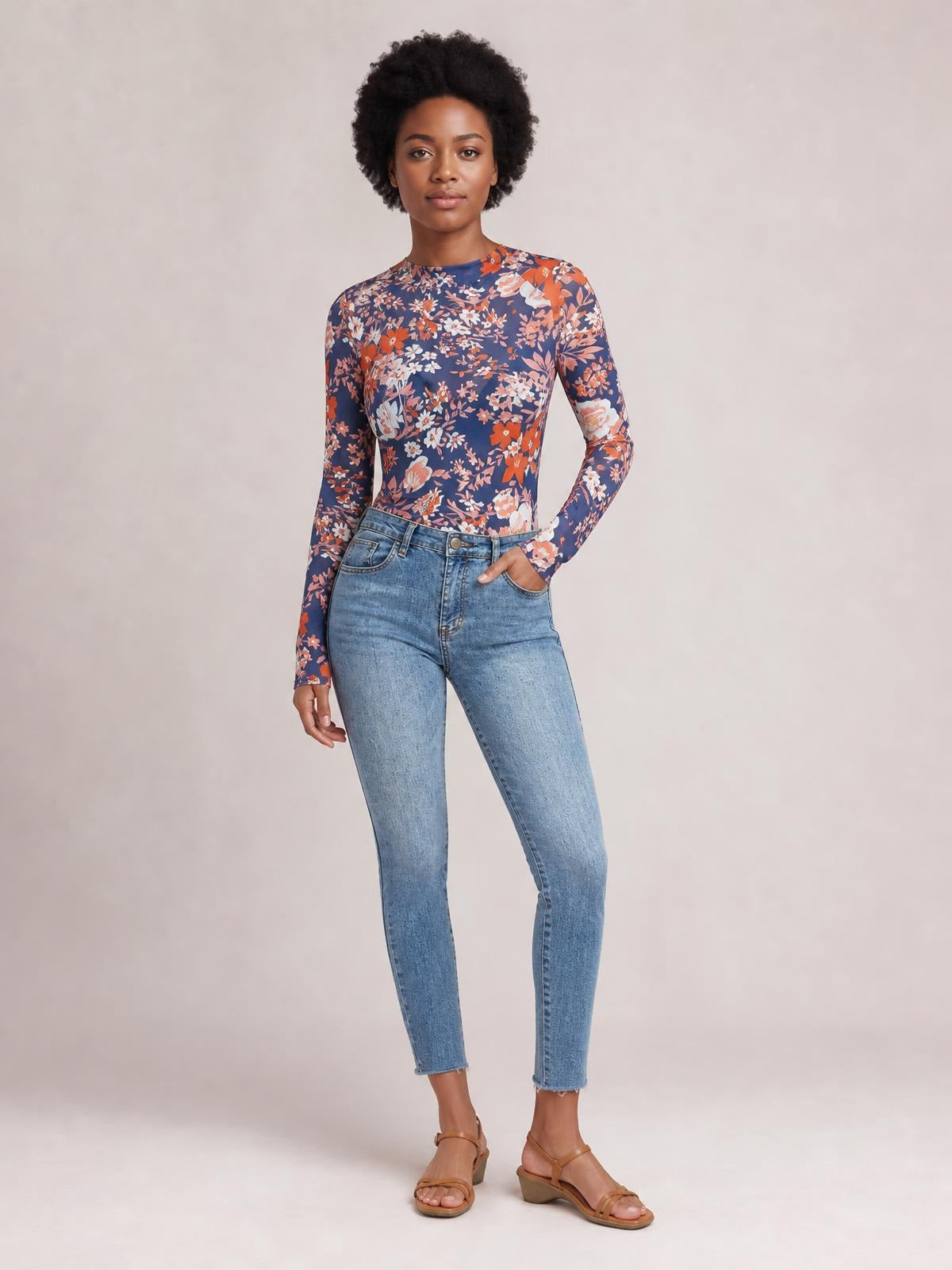 Model poses in a navy floral mock neck long sleeve top with a fitted silhouette, tucked into high-waisted jeans, one hand in a pocket.