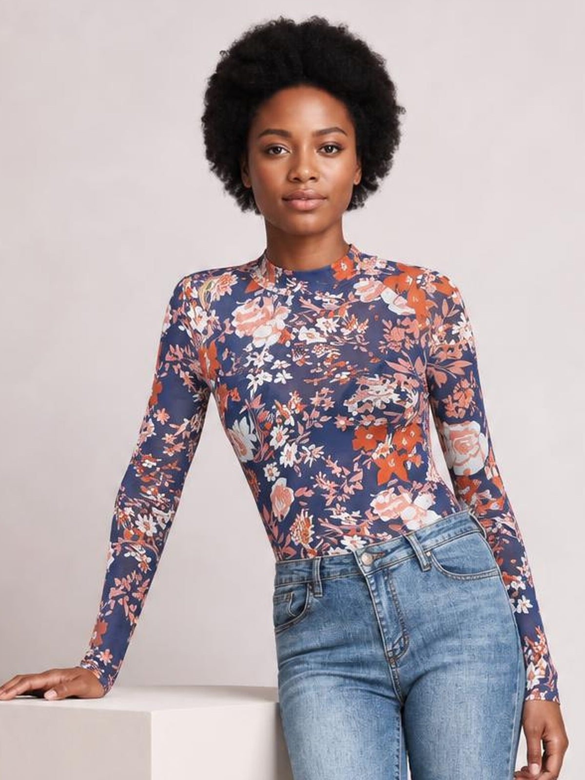 Model poses in a fitted navy Floral Mock Neck Long Sleeve Top with an allover floral print, leaning one hand on a ledge.