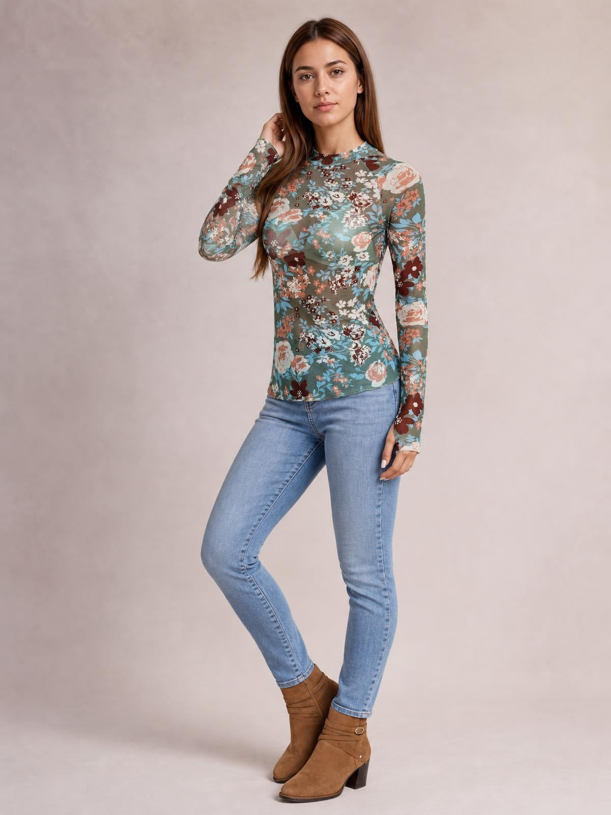 A model poses in a fitted teal floral mock neck top with long sleeves, a multicolor flower print, and a smooth, slightly stretchy silhouette.