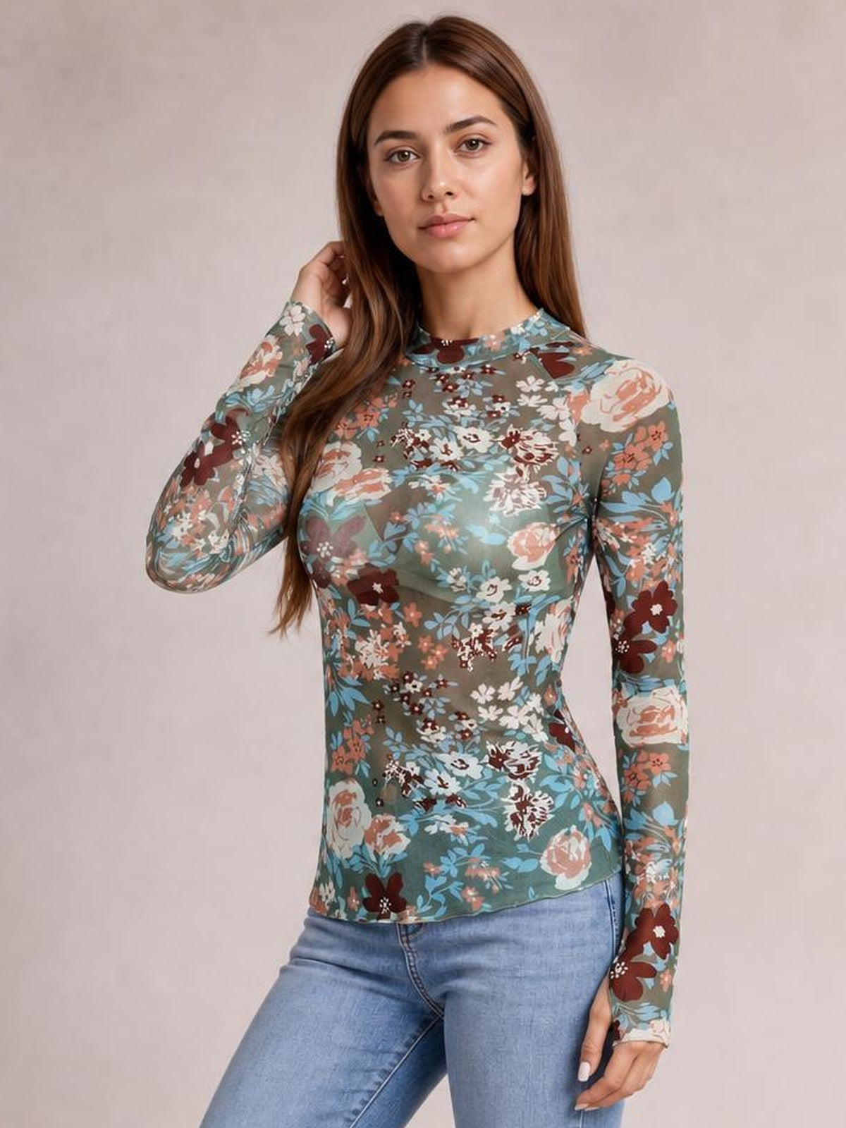 Model poses in a fitted floral mock neck long sleeve top with a muted green base, multicolor flowers, and a softly curved hem.