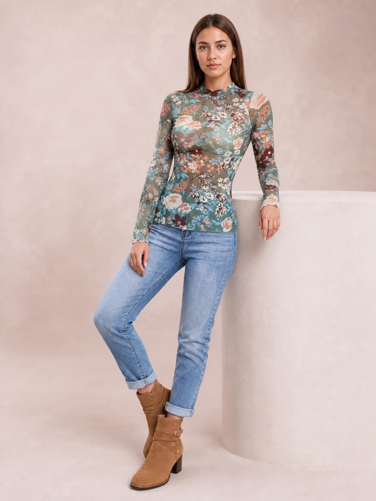Model leans against a column wearing a fitted floral mock neck long sleeve top in muted teal, burgundy, peach, and cream with a smooth stretch silhouette.