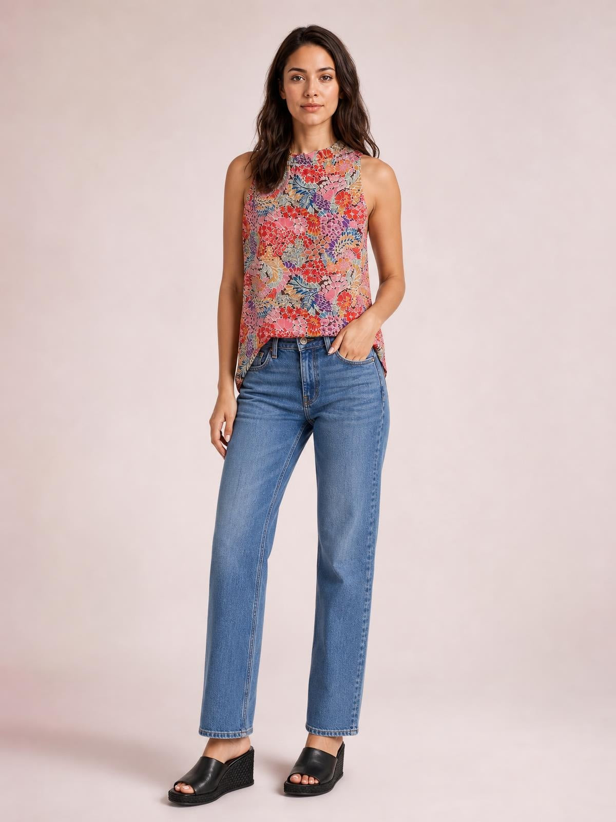 Model wears a colorful floral print mock neck tank top with a sleeveless, regular-length silhouette, standing with one hand in her jeans pocket.