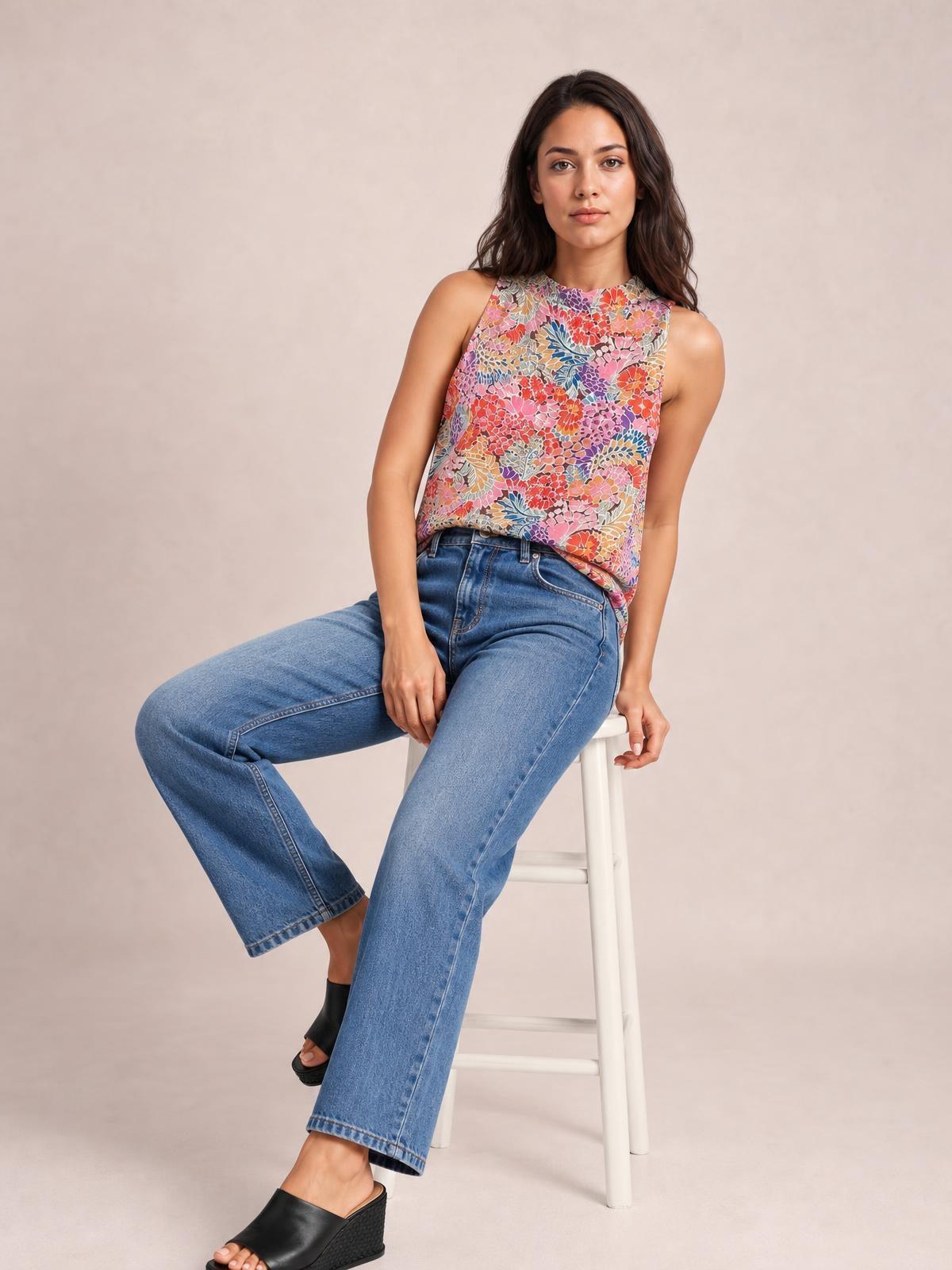 Model seated in a relaxed pose wears a colorful floral mock neck tank top with a sleeveless cut, regular-length silhouette, and clean finished edges.