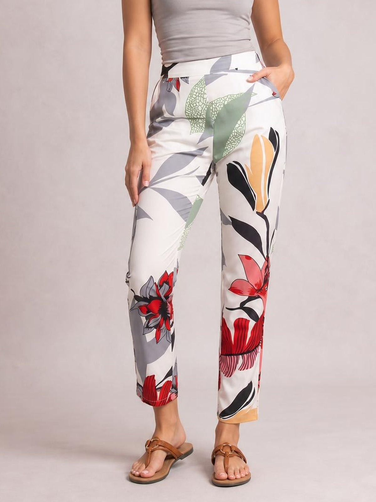Model stands with one hand in a pocket, wearing white floral print cropped pants with a colorful botanical pattern, straight-leg silhouette, and ankle-length hems.