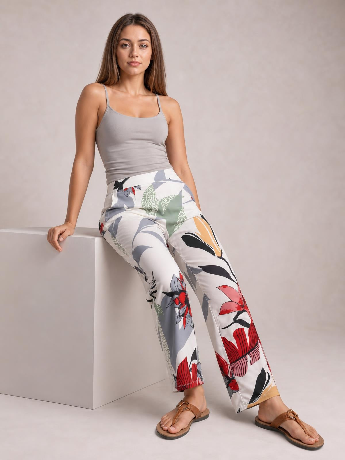 A model sits in a relaxed pose wearing white floral print cropped pants with a colorful pattern, straight-leg silhouette, and practical side pockets.