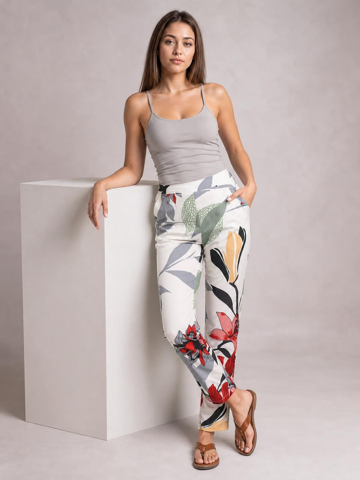 Model poses in white floral print cropped pants with side pockets, a straight-leg silhouette, and bold red, green, gray, and black botanical patterns.