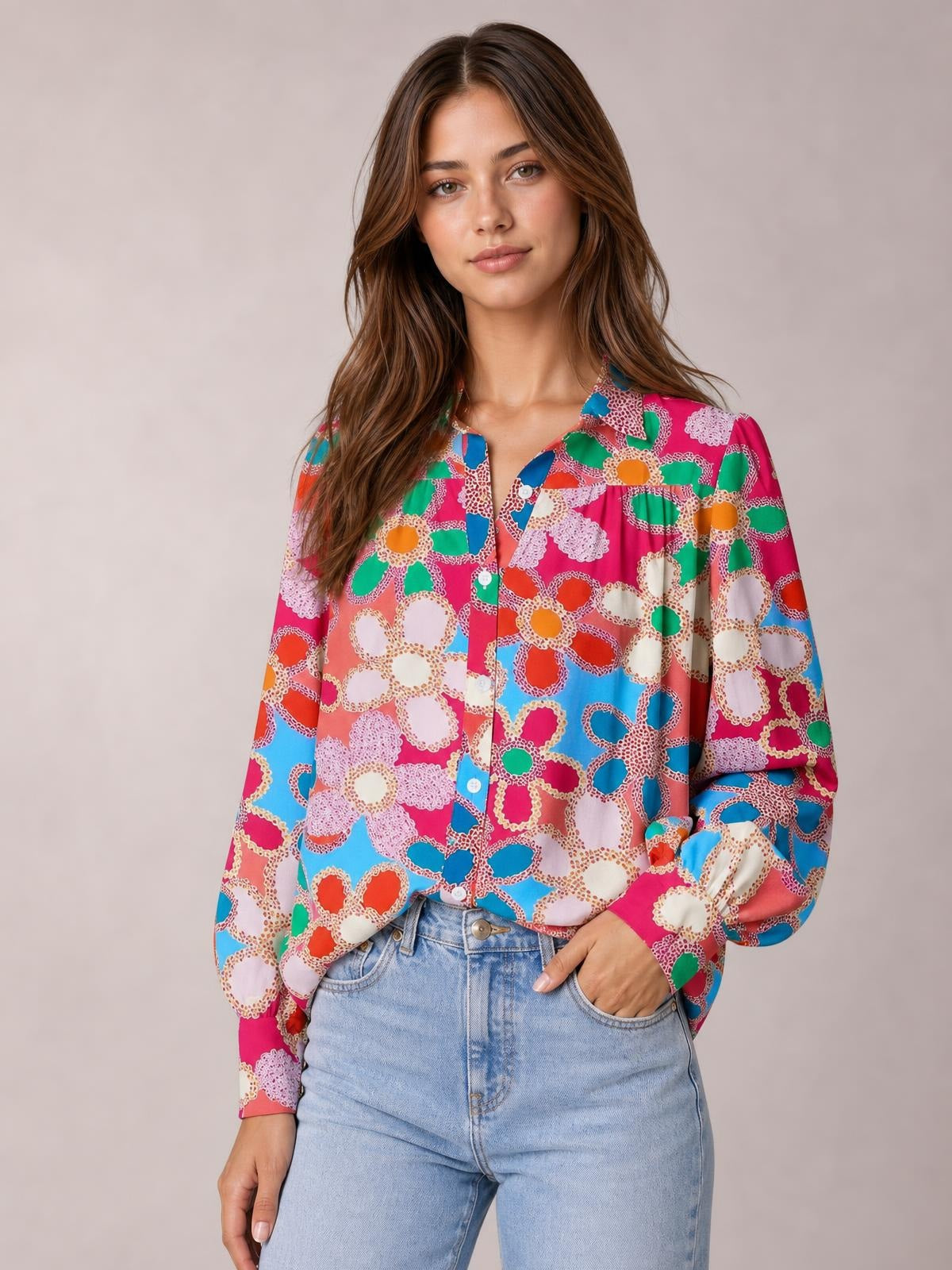 Model wearing a bright multicolor floral print shirt with a collared neckline, button front, regular length, and voluminous lantern sleeves, posing with one hand in her jeans pocket.