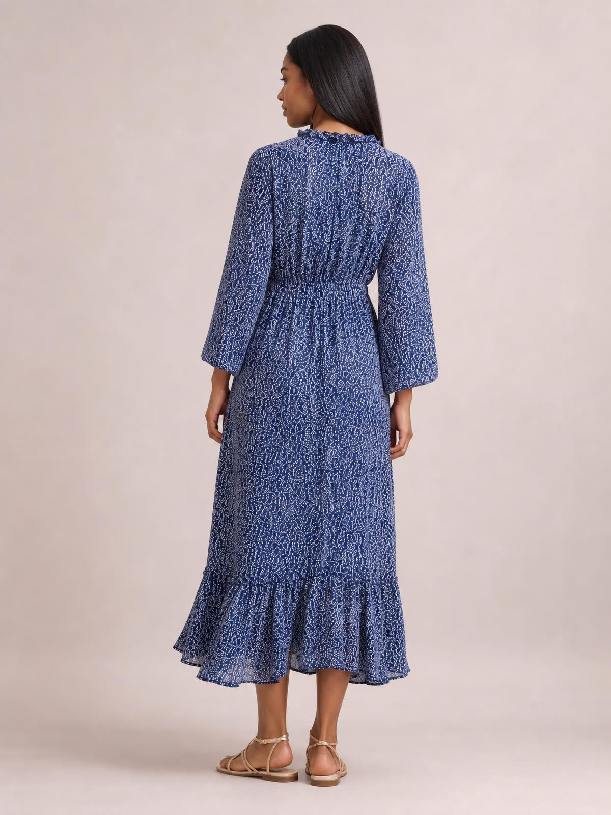 A model faces away in a navy floral print midi dress with long sleeves, a smocked waist, relaxed silhouette, and flounced ruffle hem.