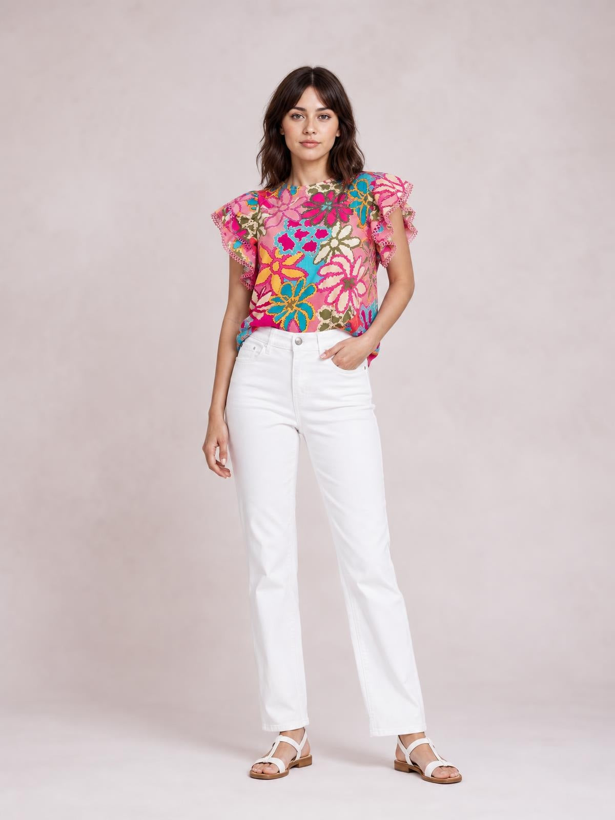 A model stands with one hand in her pocket wearing a bright multicolor floral print blouse with a round neck, short flutter sleeves, and a relaxed regular silhouette.