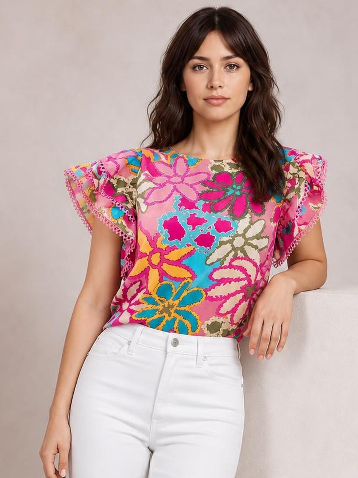 A woman poses with one hand resting at her side in a colorful floral print blouse with a round neck, short flutter sleeves, and a regular silhouette.