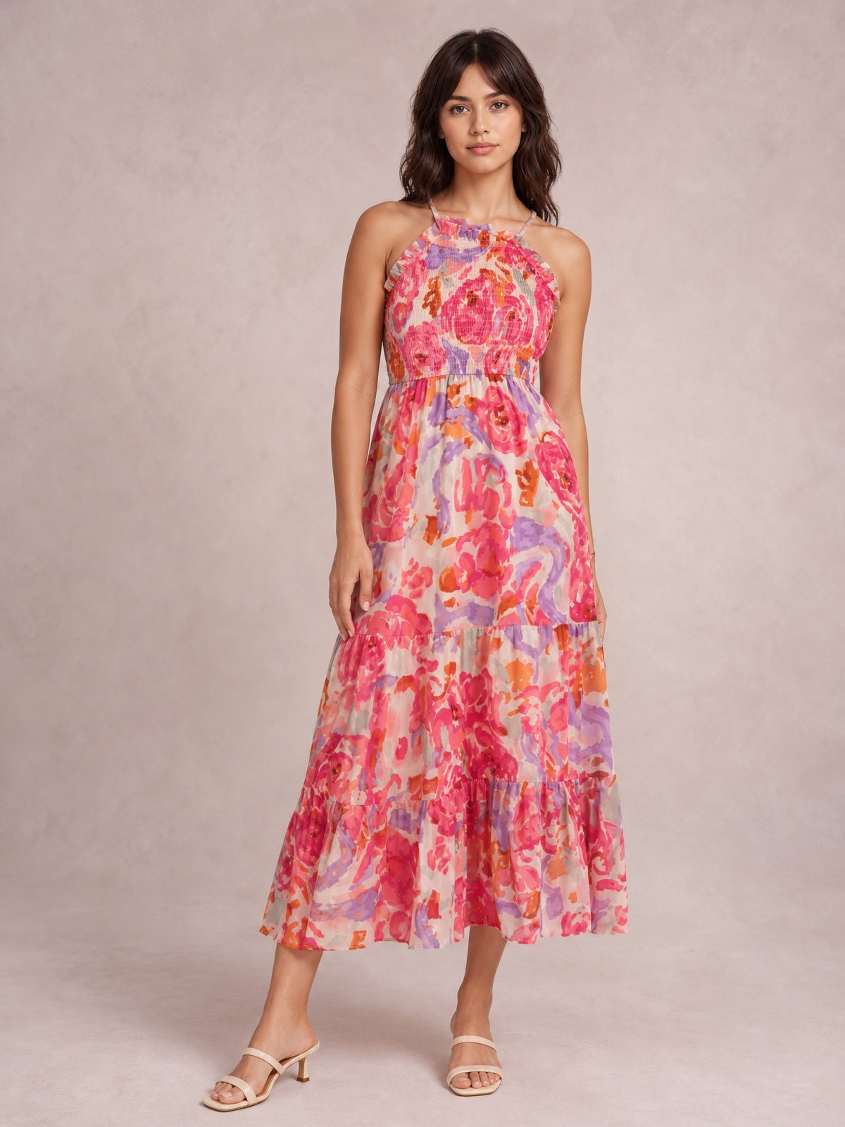 Model stands in a colorful floral print maxi dress with a smocked bodice, thin straps, defined waist, and flowing tiered skirt in pink, coral, orange, and lavender.