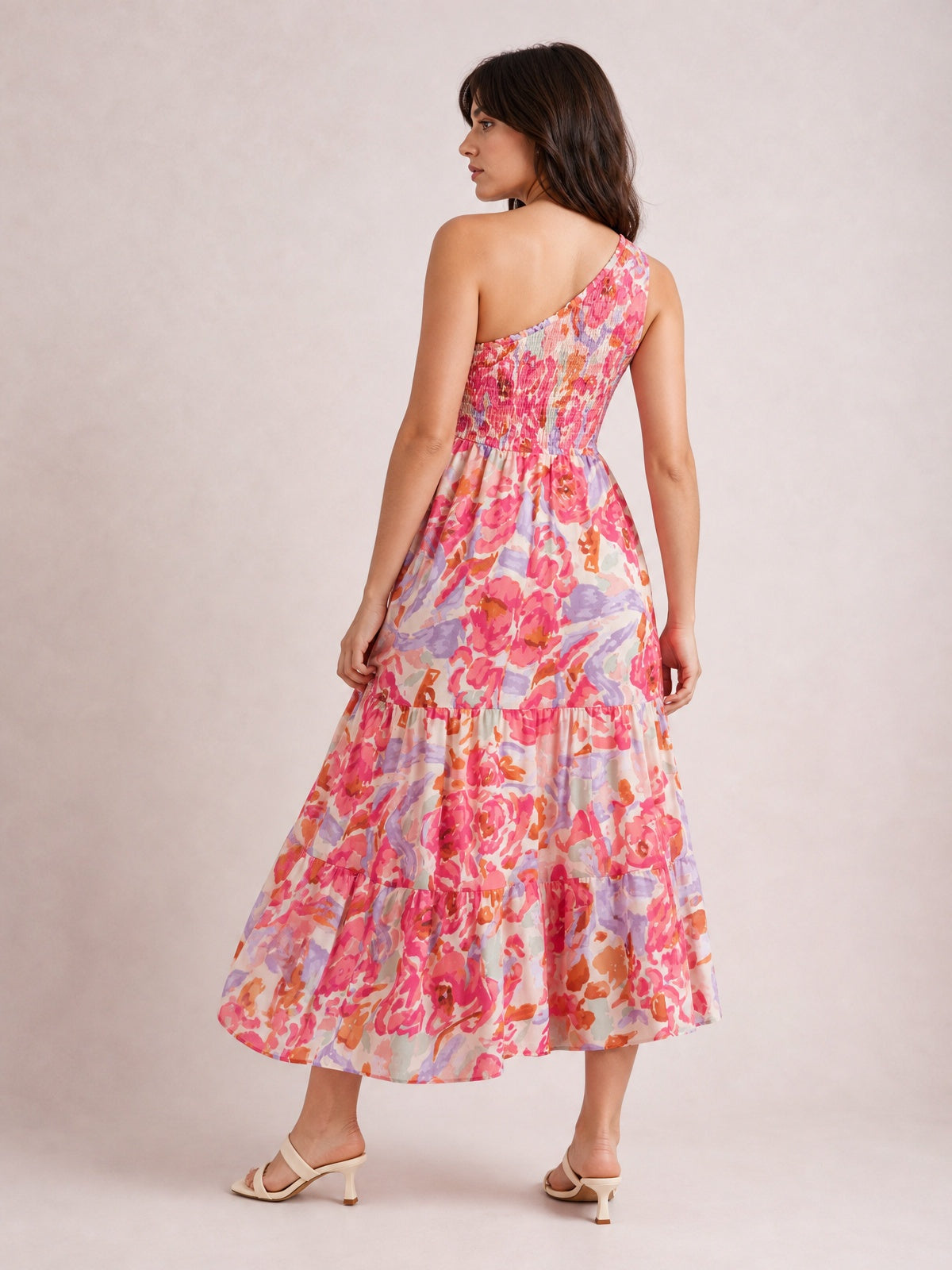 Model poses in a floral print shirred one-shoulder maxi dress with a smocked bodice, colorful pink and lavender tiers, and a flowing silhouette.