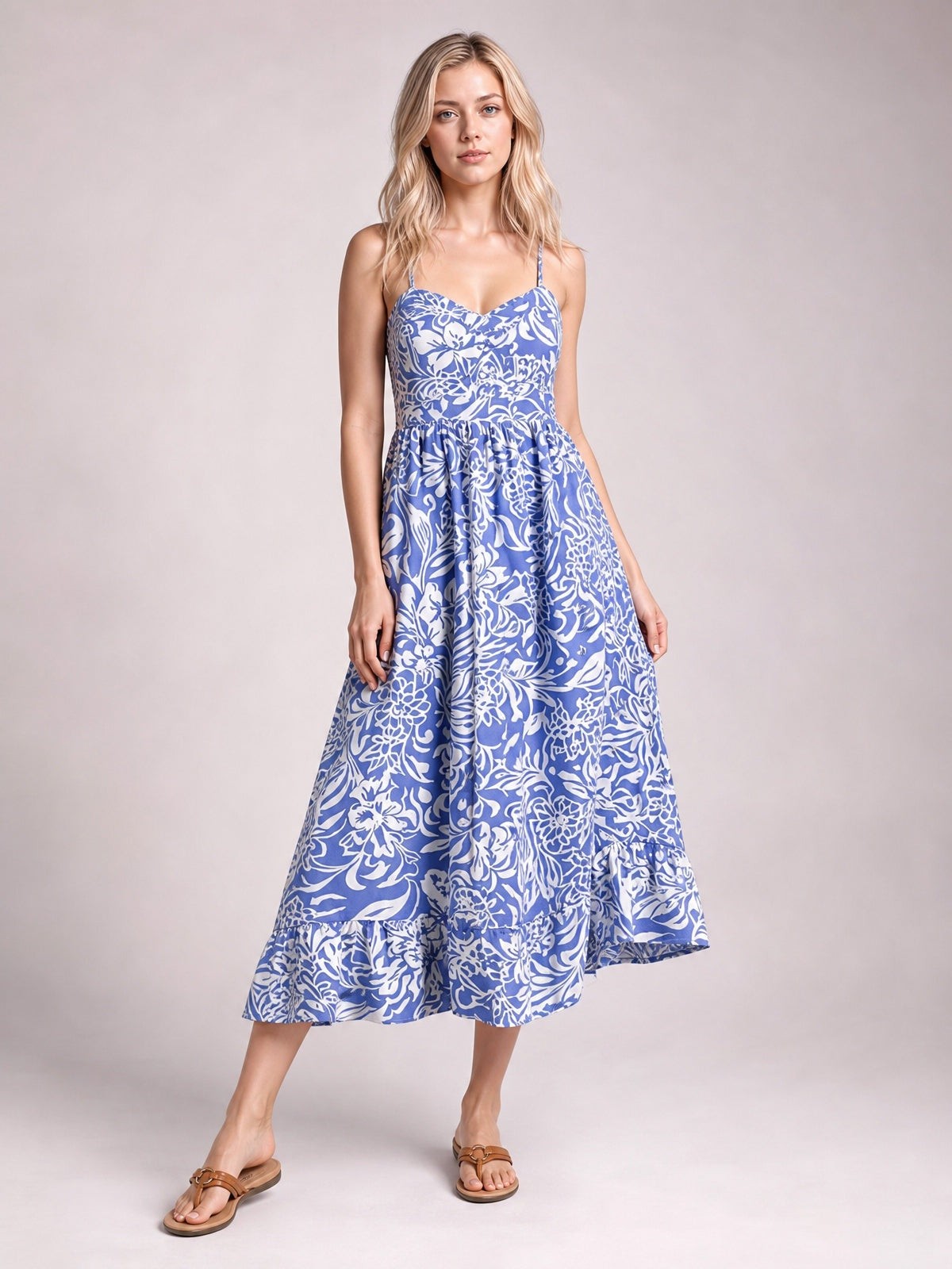 Model wears a blue and white floral print spaghetti strap high waist midi dress with a fitted bodice, flowing skirt, tiered ruffle hem, and sandals.