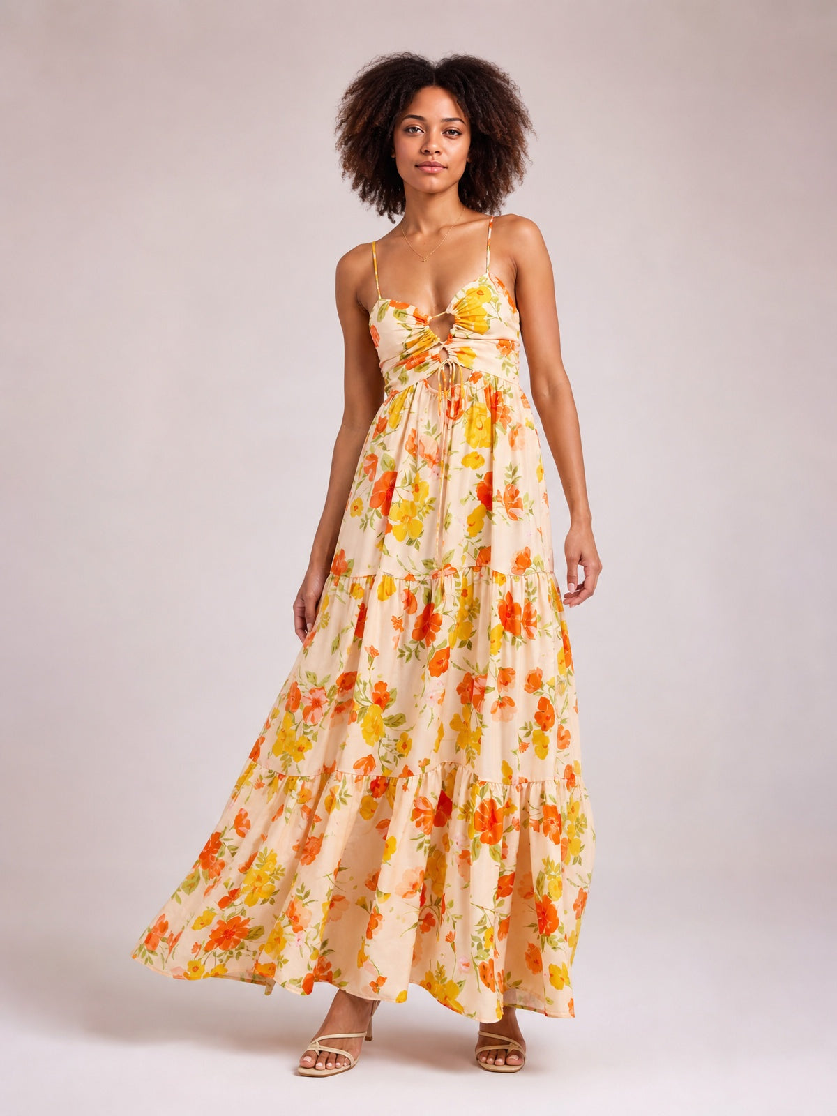 Model poses in a cream floral print tie-front maxi dress with slender straps, a cutout bodice, gathered waist, and flowing tiered skirt.