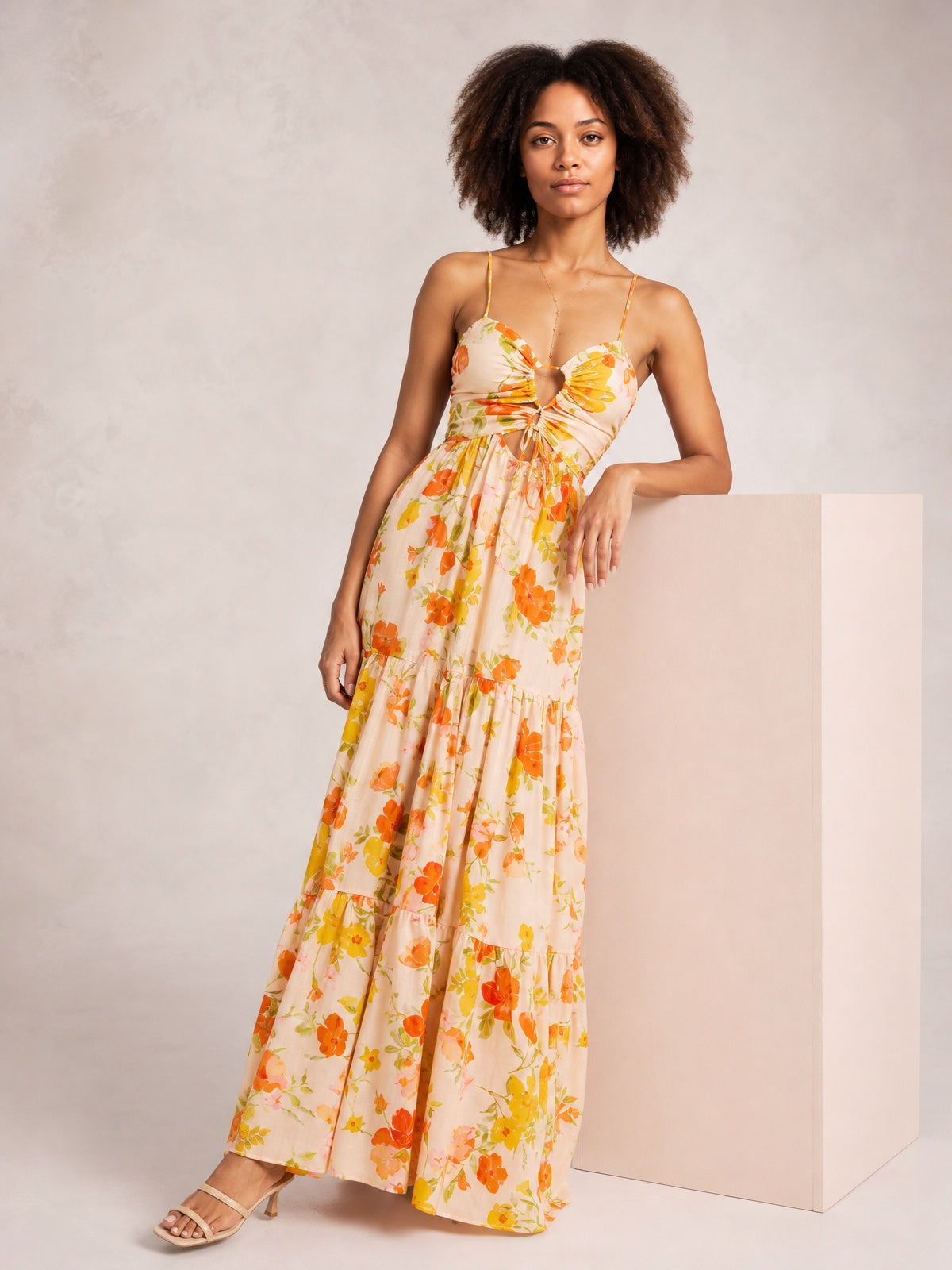 Model poses in a floral print tie-front maxi dress with slender straps, a cutout bodice, gathered waist, and flowing tiered silhouette.