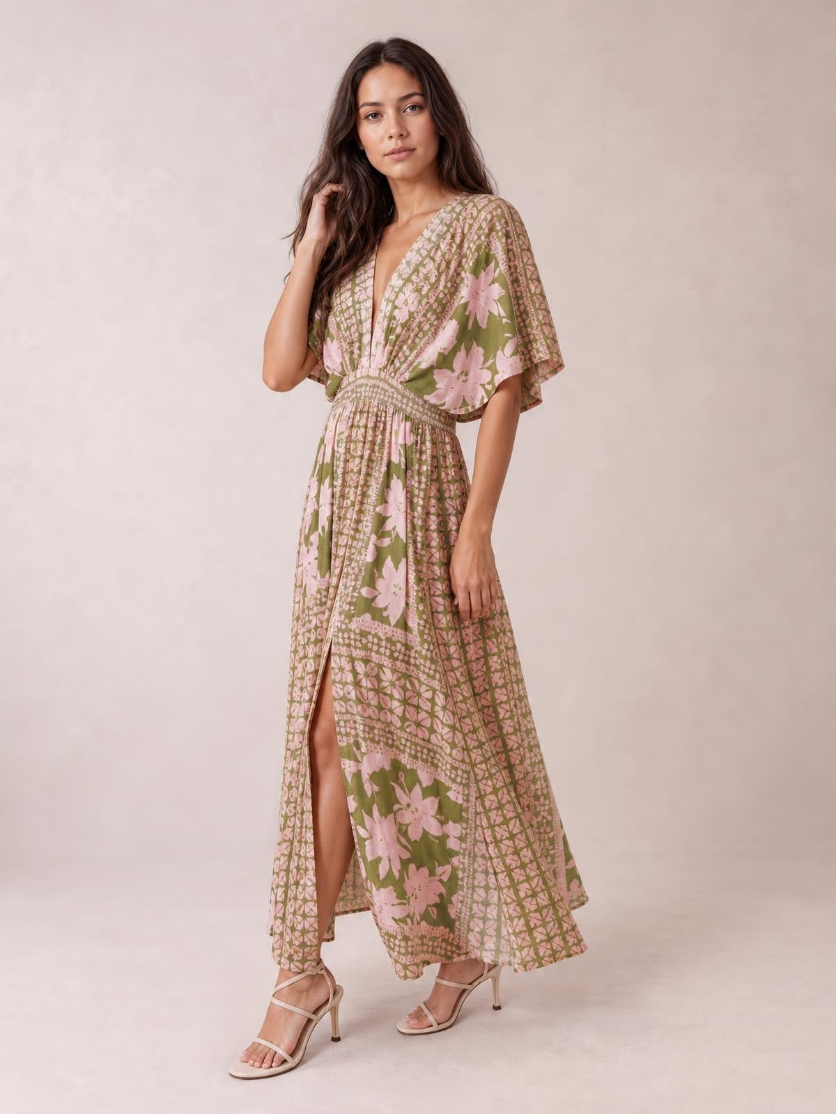 A model poses in a green and pink floral-print maxi dress with a V-neck, flutter sleeves, smocked waist, flowing silhouette, and high front slit.