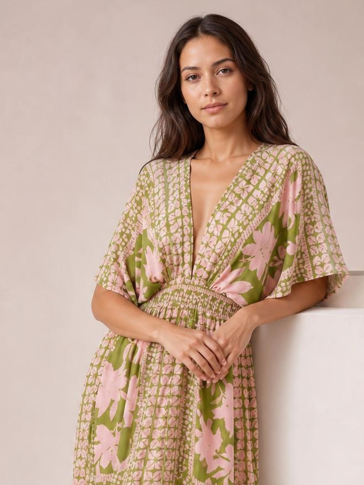 Model wearing a green and pink floral print V-neck maxi dress with a smocked waist, flowing silhouette, and short flutter sleeves, standing with hands clasped.