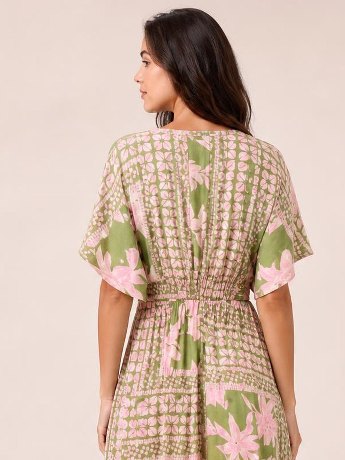 Model shown from behind in a green and pink floral print maxi dress with short sleeves, a smocked waist, and a flowing floor-length silhouette.