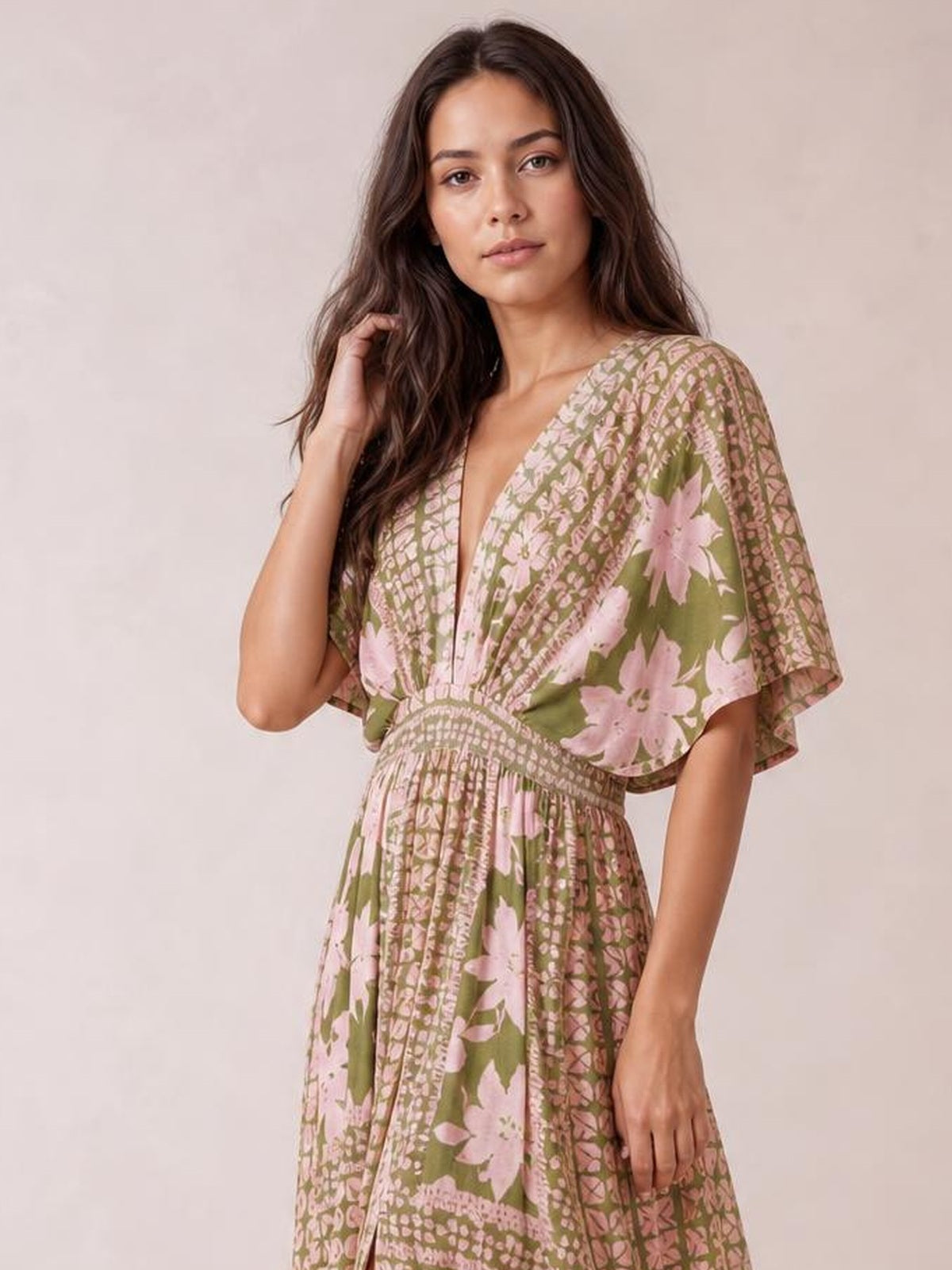 Model touches her hair while wearing an olive green and pink floral print maxi dress with a V-neck, flutter sleeves, smocked waist, and flowing silhouette.