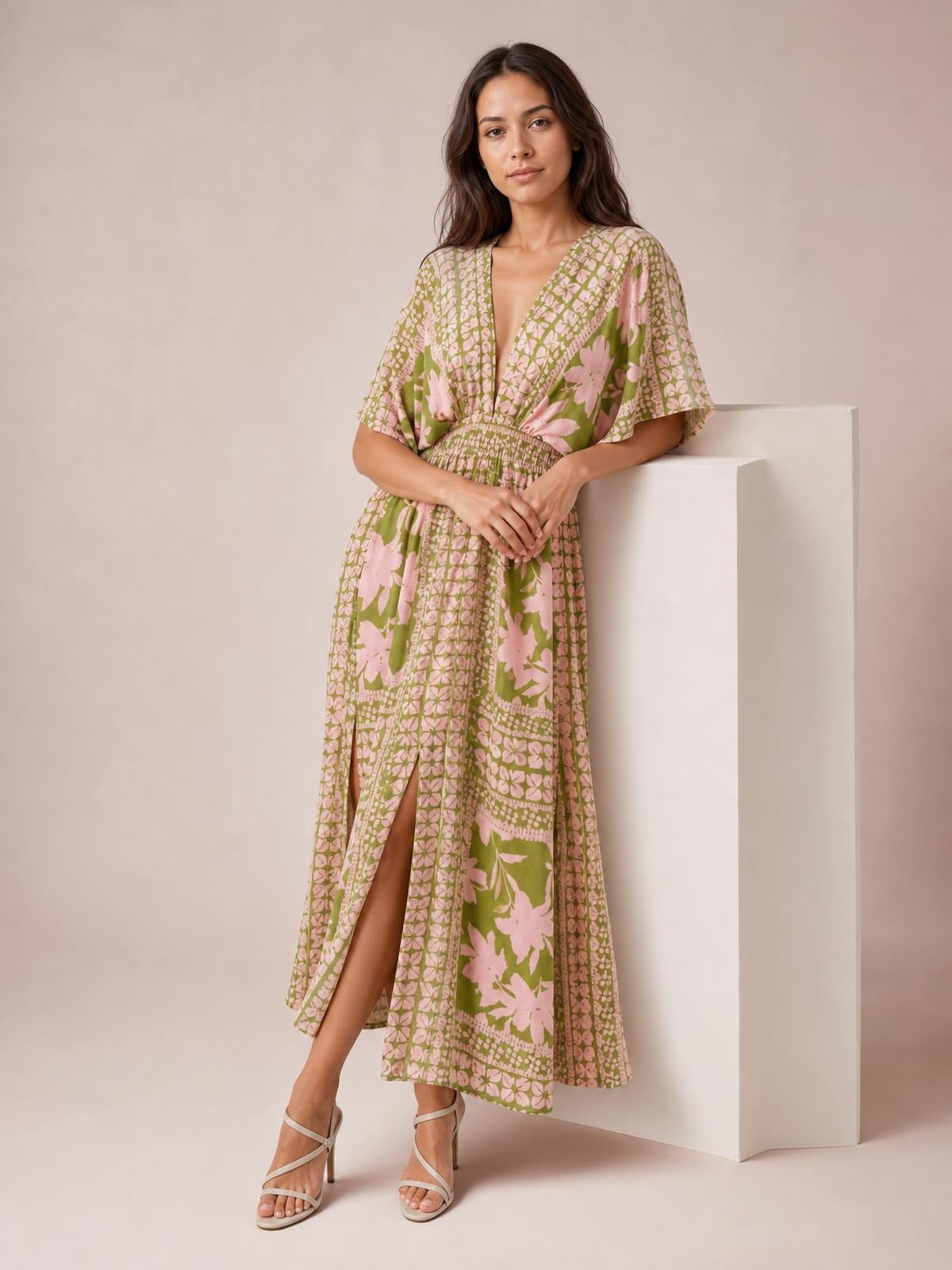Model stands with hands clasped in a green and pink floral print V-neck maxi dress featuring short sleeves, a smocked waist, and a high front slit.