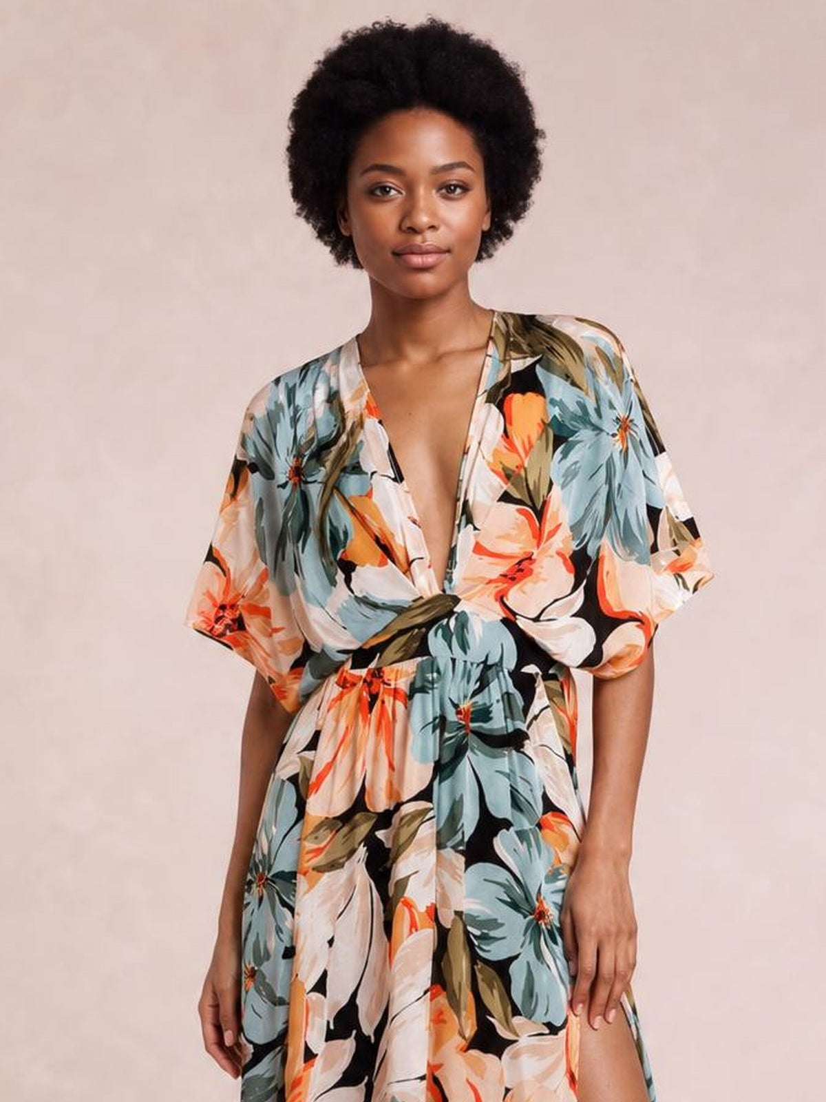 Model poses in a floral print maxi dress with a deep V-neck, twisted waist, short sleeves, and a flowing silhouette in blue, peach, white, and black.