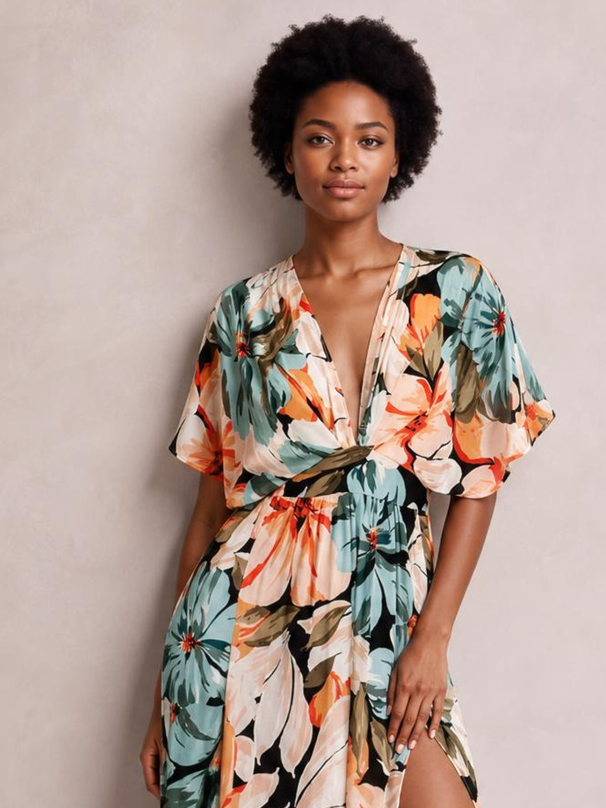 A model stands in a colorful floral-print V-neck maxi dress with flutter sleeves, a twisted waist, flowing silhouette, and high side slit.