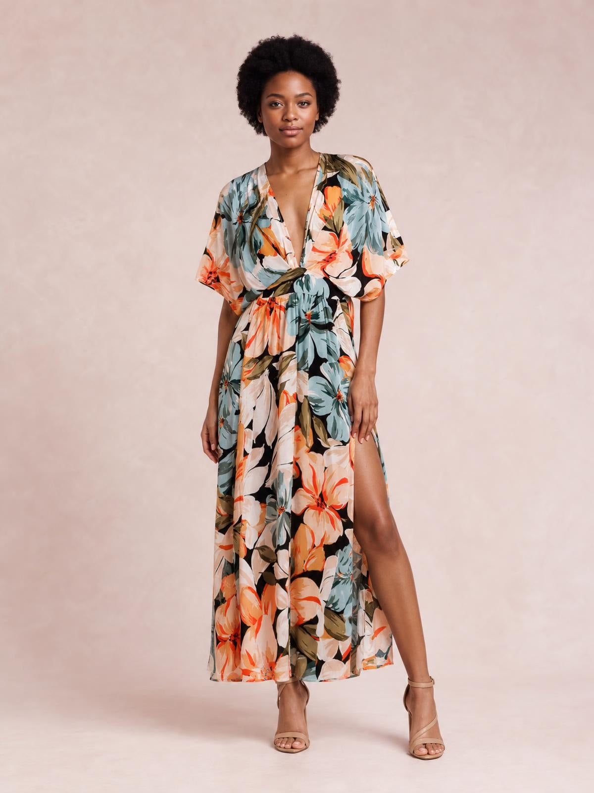 A model stands in a multicolor floral print maxi dress with a deep V-neck, twisted gathered waist, flowing silhouette, short sleeves, and a high side slit.