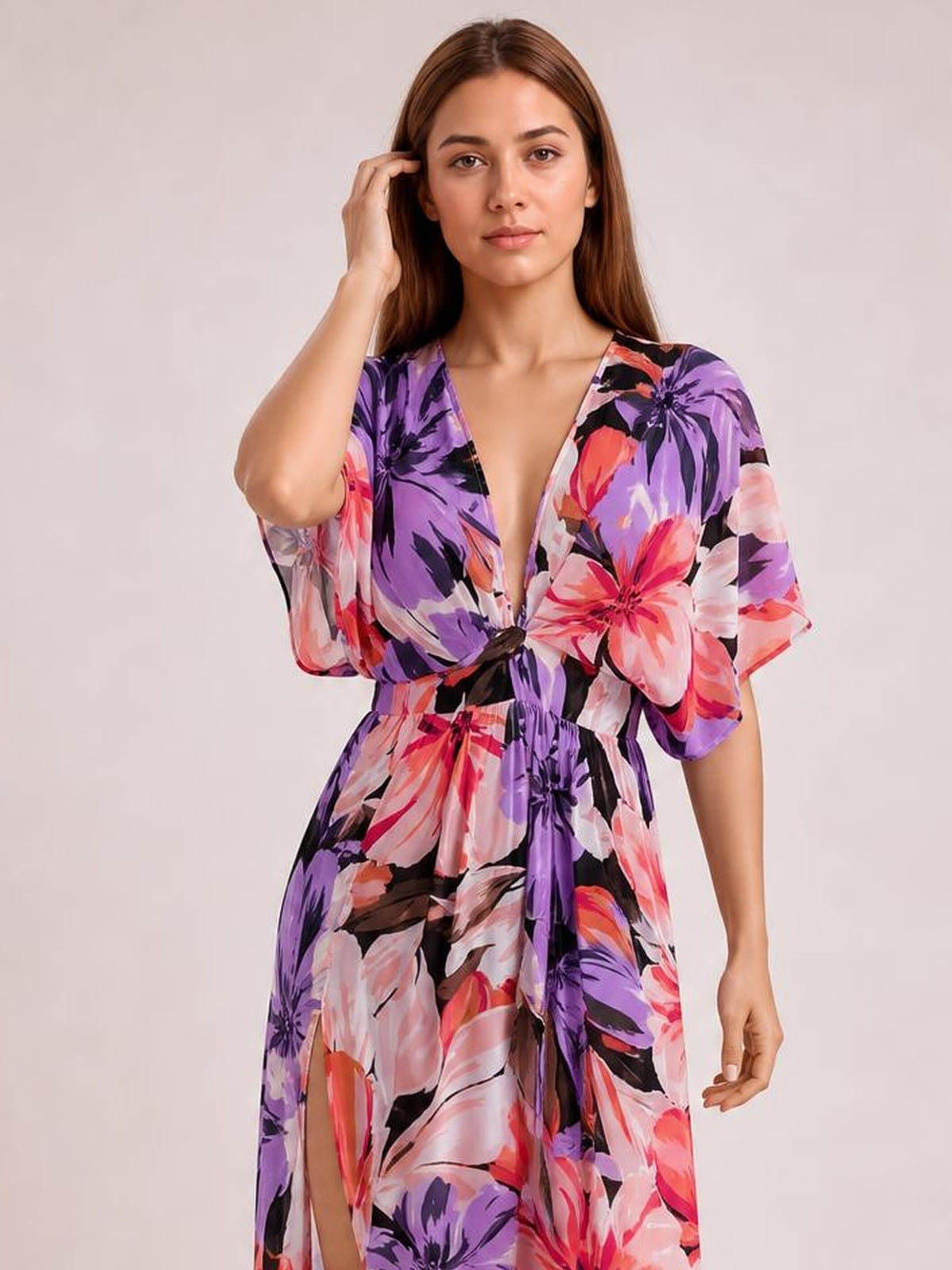 A model poses in a vibrant purple, pink, and black floral print maxi dress with a deep V-neck, twisted waist, flowing silhouette, and high side slit.