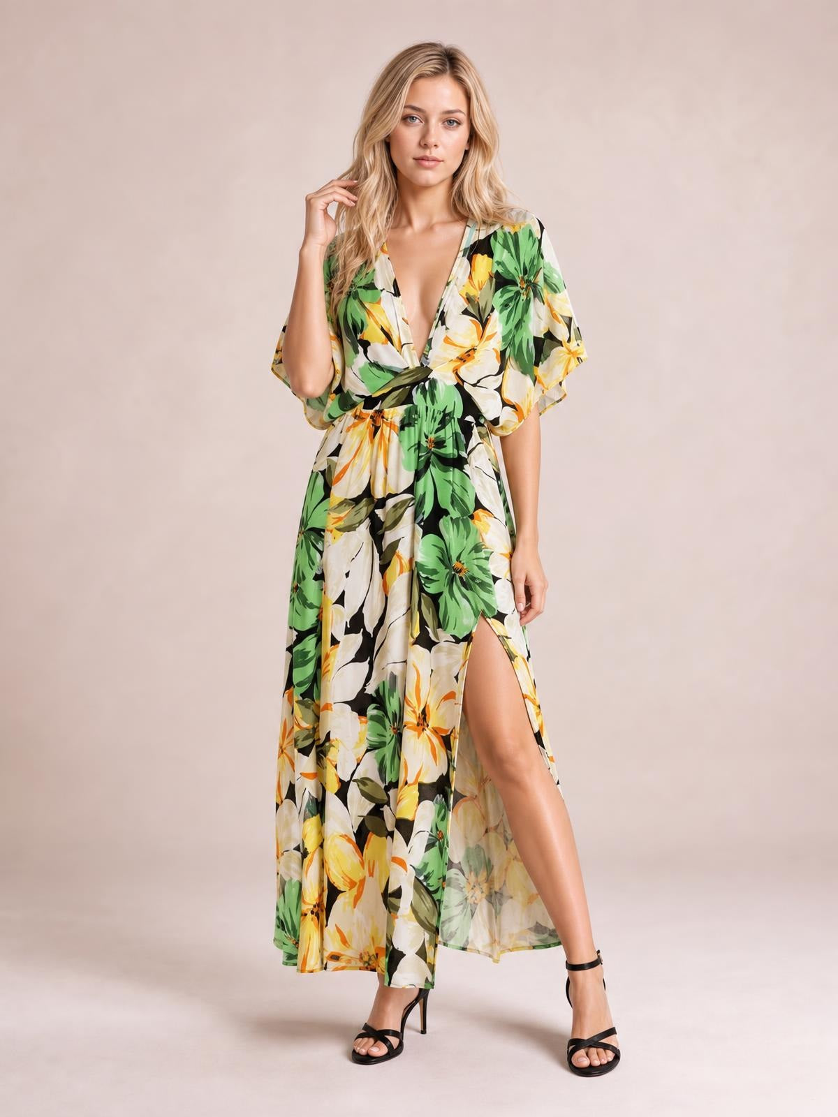 A model poses in a green, yellow, and white floral print V-neck maxi dress with flutter sleeves, a twisted waist, flowing silhouette, and high side slit.