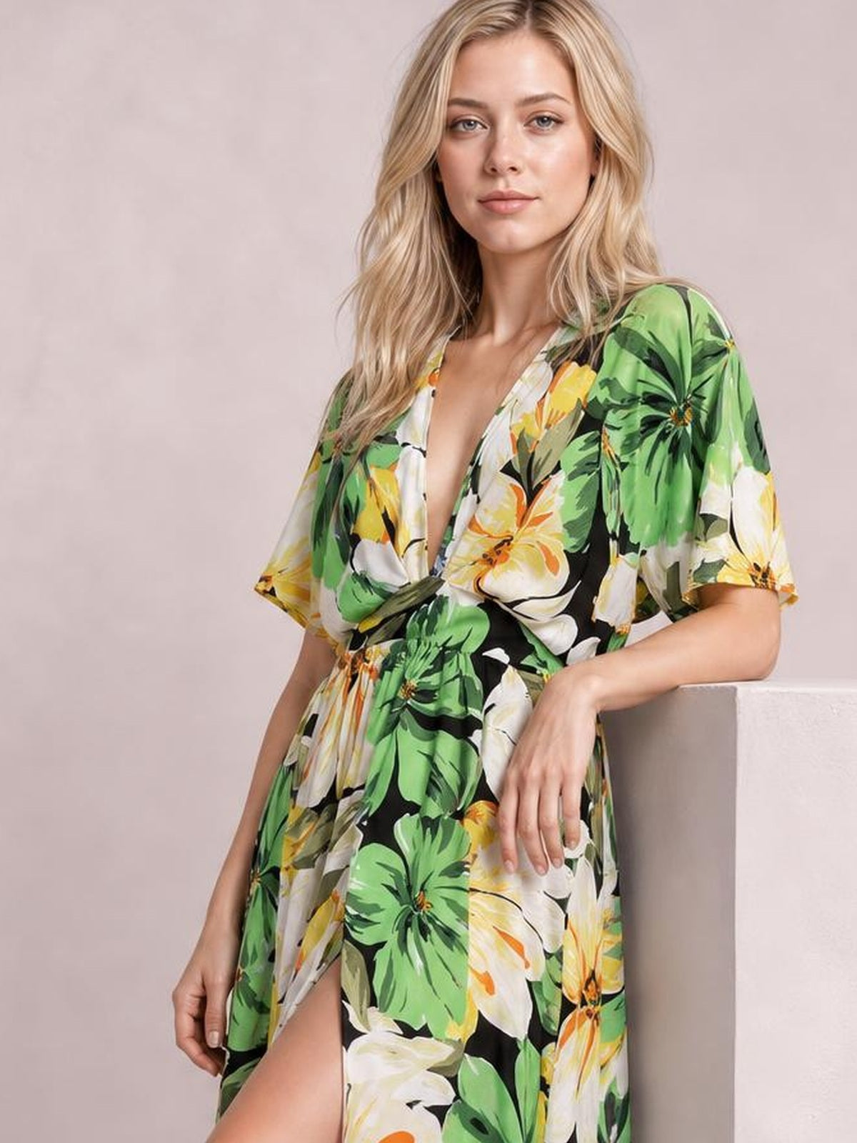Model poses in a green, black, white, and yellow floral print maxi dress with a V-neck, twisted waist, flowing silhouette, and high front slit.