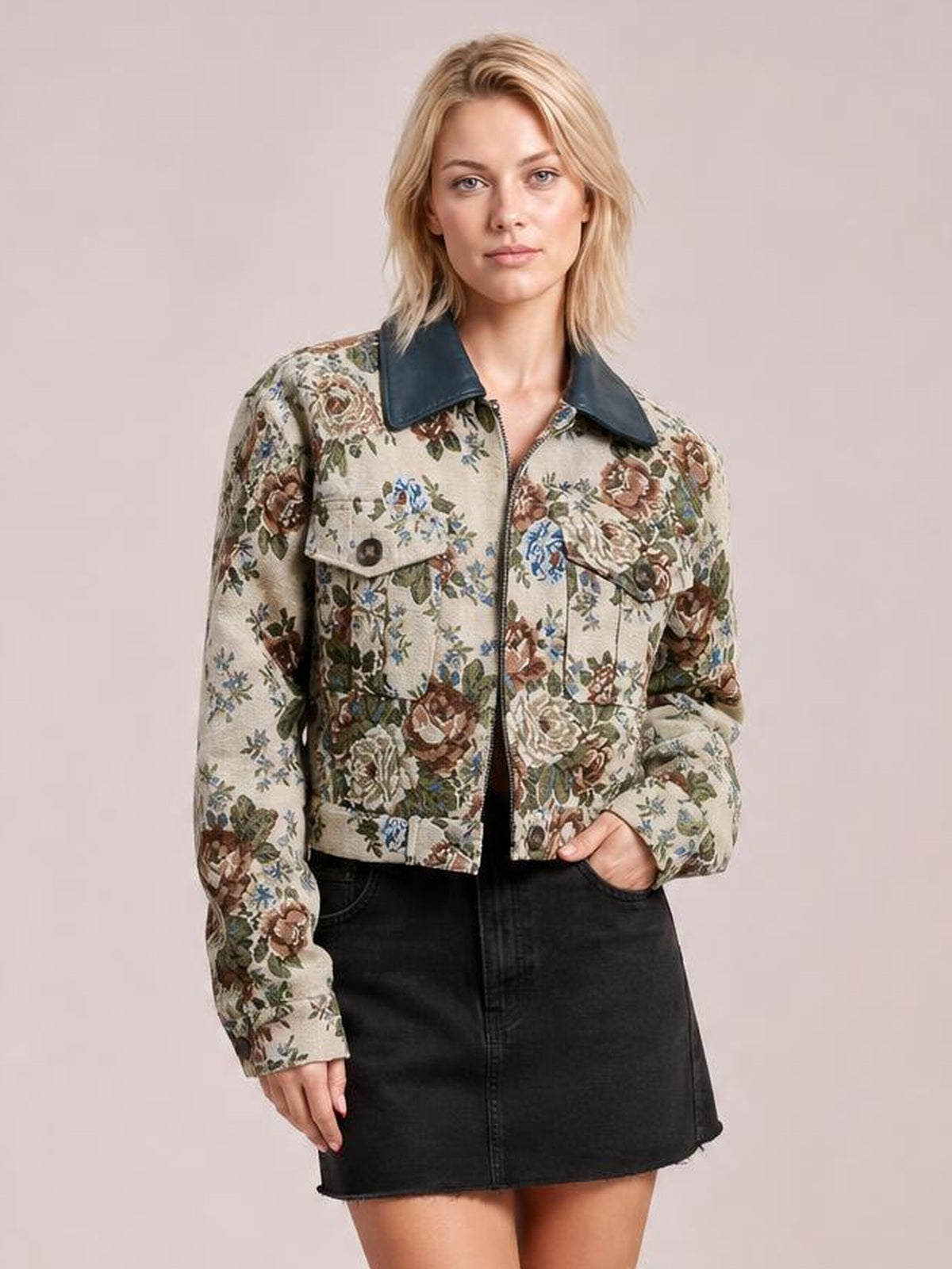 Model wears a beige floral print zip-up jacket with a dark contrast collar, buttoned chest pockets, cropped silhouette, and one hand tucked into a pocket.
