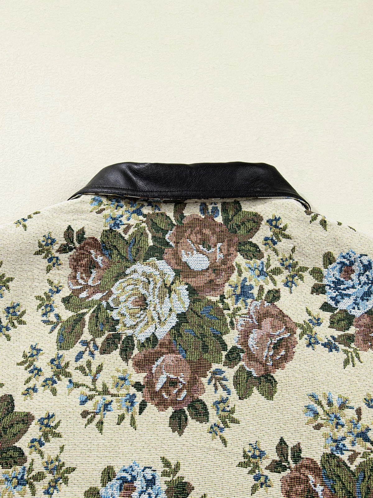 Close-up view of a cream floral-print jacket with a structured black contrast collar and colorful rose-and-leaf pattern.