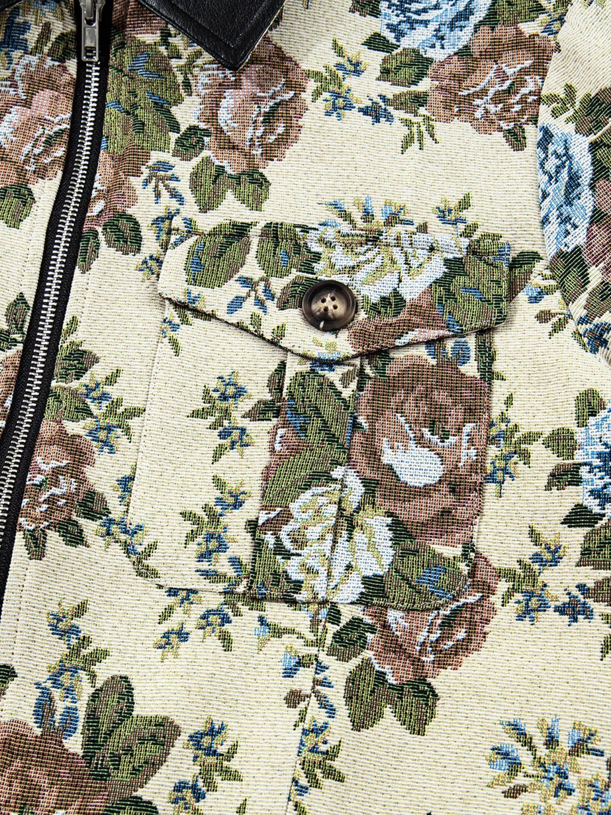 Close-up of a floral print jacket in cream, green, blue, and brown with a contrasting black collar, zip front, buttoned pocket, and visible woven construction.