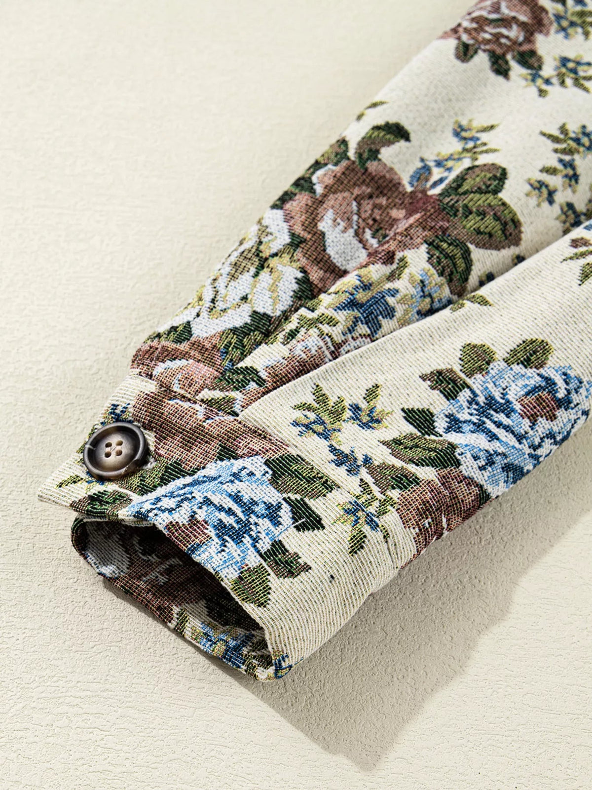 Close-up of a floral print jacket sleeve shows multicolored flowers, a folded cuff, and a dark button securing the tailored construction.