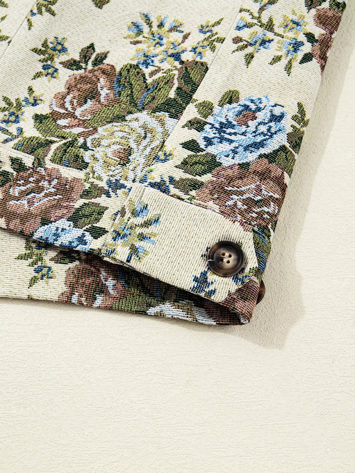 Close-up of a floral print jacket sleeve and buttoned cuff in cream, blue, brown, and green with textured woven construction.