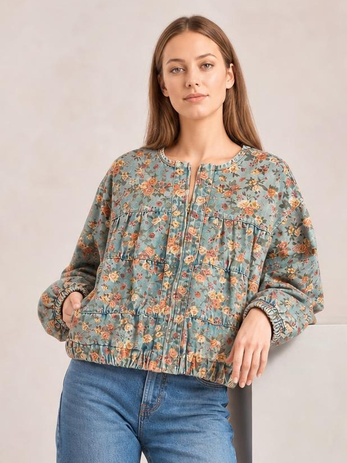 Model wearing a blue floral print denim jacket with a cropped silhouette, round neckline, front zipper, elastic cuffs and hem, and relaxed sleeves.