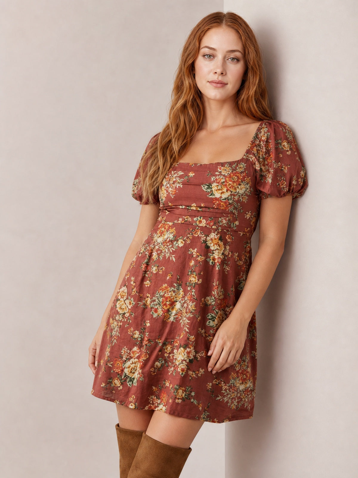 Model wearing a rust floral mini dress with a square neckline, puff sleeves, fitted bodice, and gently flared skirt, posed leaning against a wall.